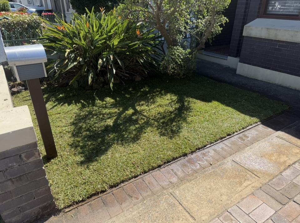The same front yard with fresh new turf and a neat edge along the brick path